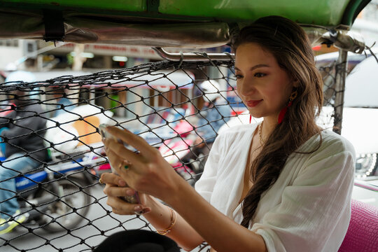 A woman uses a phone on a tuk-tuk in Bangkok