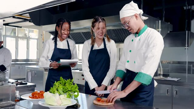 4K, Two female students learn to cook because interested in becoming chef. Male chef standing teaching students how to cut tomatoes Let's see how to cut it comes out beautiful and not messy.