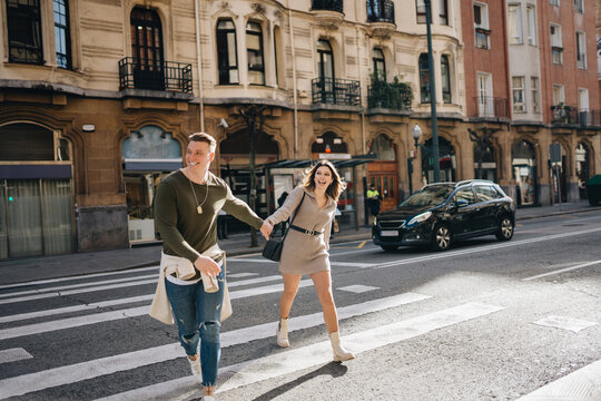 Joyful couple holding hands on pedestrian crossing