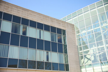 A sleek and modern building exterior with clean lines and large windows that reflect the blue sky. The building features a mix of concrete, steel, and glass, a futuristic and sophisticated look 