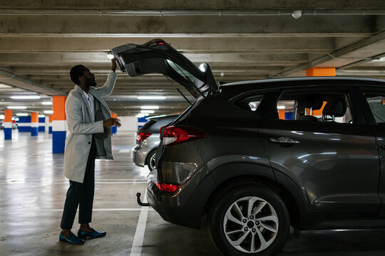 Black businessman standing in parking near car