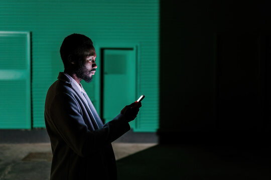 Bearded man with phone in shadow on dark street