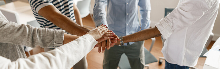 Happy group of multi ethnic coworkers stacked hands together as concept of corporate unity