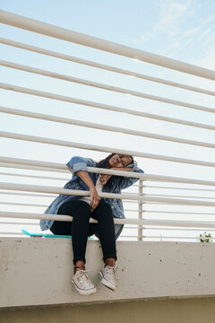 Girl with a skateboard sits with her legs dangling