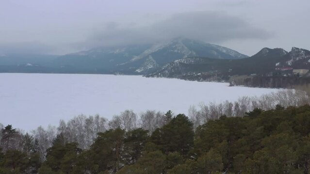 This stock video shows a winter landscape: a frozen lake, snow-capped mountain peaks, evergreen pines. This video will decorate your projects related to nature, winter landscapes, weather.