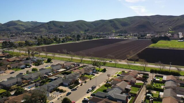 2023 - Excellent aerial footage of cars driving through a residential area by farmland in Lompoc, California.