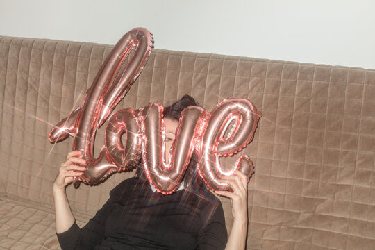 An attractive girl hides and looks out behind a Love balloon