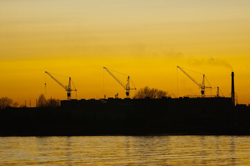 Obraz premium silhouettes of construction cranes and pipes of the plant against the background of the evening sky