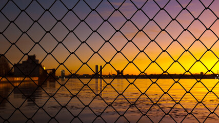 sunset, in the photo there is a metal mesh chain-link, in the background the silhouettes of city buildings