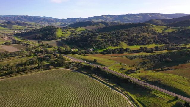 2023 - Excellent aerial footage of cars driving past farmland and green hills in Lompoc, California.