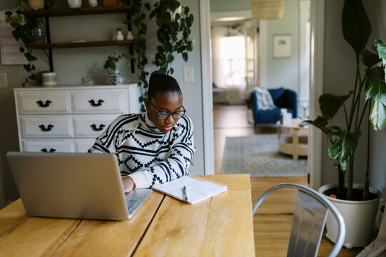 Black girl at home at kitchen table doing homework with laptop 