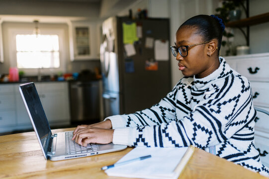 Black girl at home at kitchen table doing homework with laptop 