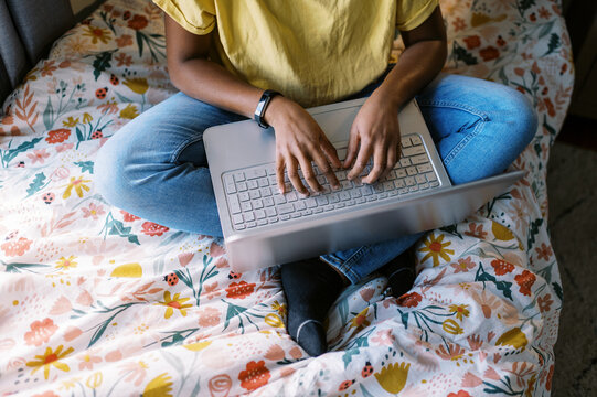 Young smiling black girl sitting on her bed in her room with laptop