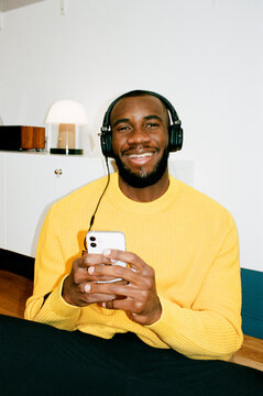 A black man in a yellow sweater listens to music with headphones