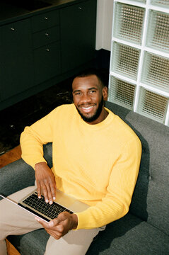 A black man works at a laptop in his apartment