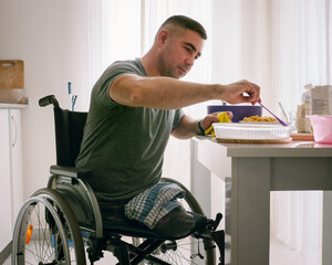 A man without legs in a wheelchair cooks in his kitchen 