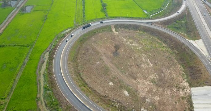 Top view of the drone, The parallel path between the green rice fields and dry fields, car drive on circle shape road leading to the main road.