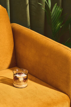 Latte on mustard couch in front of green curtain and plant. 