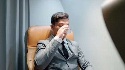 Asian businessman wearing suit sitting in seat on the plane receiving drinking water from the flight attendant on airplane