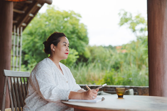 Curve Asian woman sitting and writing down ideas on a terrace