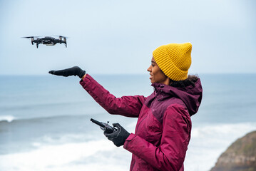 Naklejka premium black woman tourist operating drone above ocean