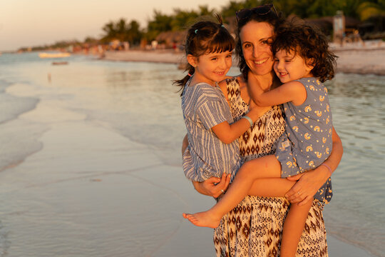 Happy woman holding daughters on beach - Powered by Adobe