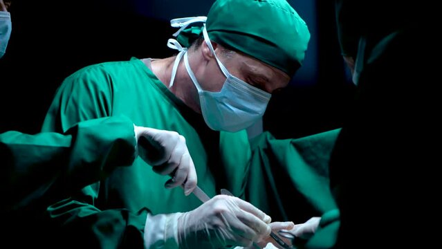 4K, Close-up doctor's face hand doctor doing breast surgery man lying on operating bed, doctor had serious expression on surgery, nurse soaks up blood from surgery cuts knife closely into skin.