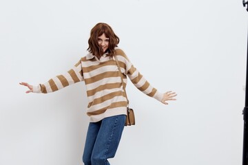 a joyful, funny woman poses energetically with her arms outstretched in stylish clothes, standing on a white background holding a beige bag on her shoulder
