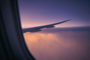 View from window of airplane during flight above clouds at dawn. Selective focus on aircraft wing..