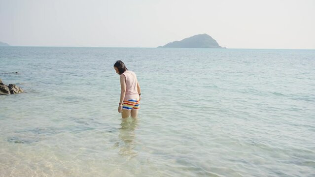 Young Asian woman in walking and playing on tropical beach at summer sunset. Happy female enjoy and fun outdoor activity lifestyle on holiday travel vacation at the sea