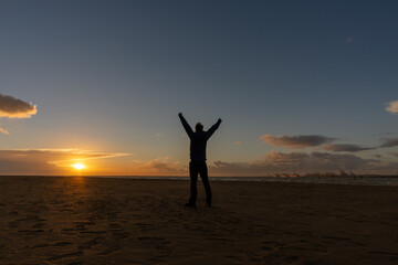 Fototapeta na wymiar Young man, standing, raising his arms, watching the sunset on beach