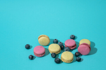 Colorful french macaroons and blueberries on a blue background