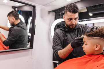 Latino barber focused lining up mixed race boys edges during haircut