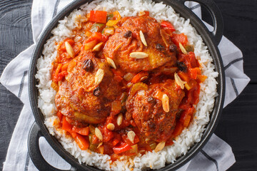 Country Captain chicken fried and then stewed with vegetables, raisins, almonds, tomato sauce and curry, served with rice in a pan on the table. Horizontal top view from above
