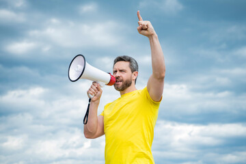 man in yellow shirt agitate in loudspeaker on sky background - obrazy, fototapety, plakaty
