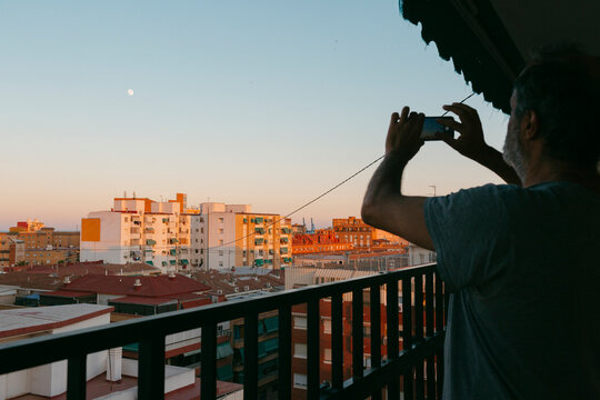 Man taking picture of full moon over city from terrace at sunset
