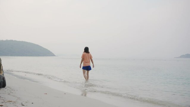 Young Asian woman in walking and playing on tropical beach at summer sunset. Happy female enjoy and fun outdoor activity lifestyle on holiday travel vacation at the sea