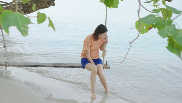 Young Asian woman was playing on a swing on a beautiful beach.