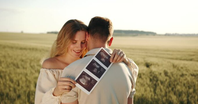 Young couple holding ultrasonography image while hugging in the field