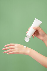 A white tube without label is held in woman model’s hand with a cream texture on another hand....