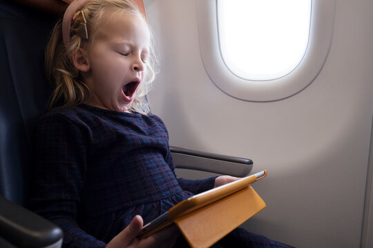 Cute blonde girl with tablet yawning in plane