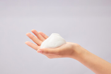 A beautiful female hand with white cleanser foam texture displayed on. Skin care and cleansing,...