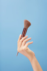 A beautiful hand model is carrying an angled brush over a light blue background. Cosmetic product promotion