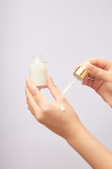 Woman drops serum on her hand. Holding an unlabeled serum bottle on a light background. Scene for advertising cosmetic product, mockup for package design