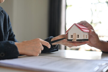 Fototapeta na wymiar Shot of realtor selling with house model offering to client, bank worker offers loan, making purchasing deal,