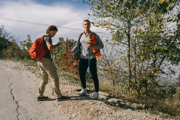 Young strong hikers standing on a road in the mountain with hiking sticks in their hands