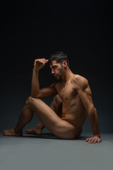 Back view of a smooth naked seductive man sitting on the floor in a studio, isolated on black
