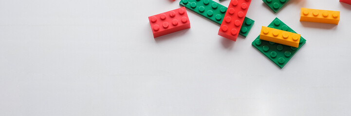 Top view on multicolor toy bricks on white wooden background. Children toys on the table.Developing children games frame.web banner. copy space. Colorful plastic bricks