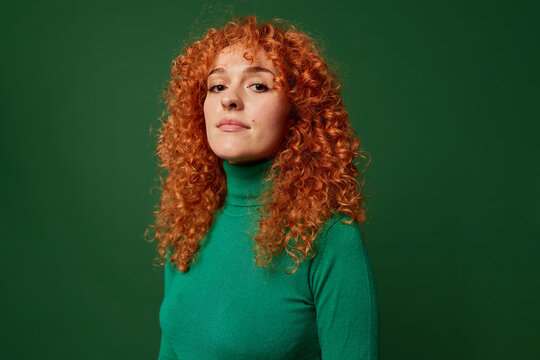 Self assured young ginger woman on green background
