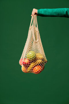 Crop woman holding string bag with fruits
